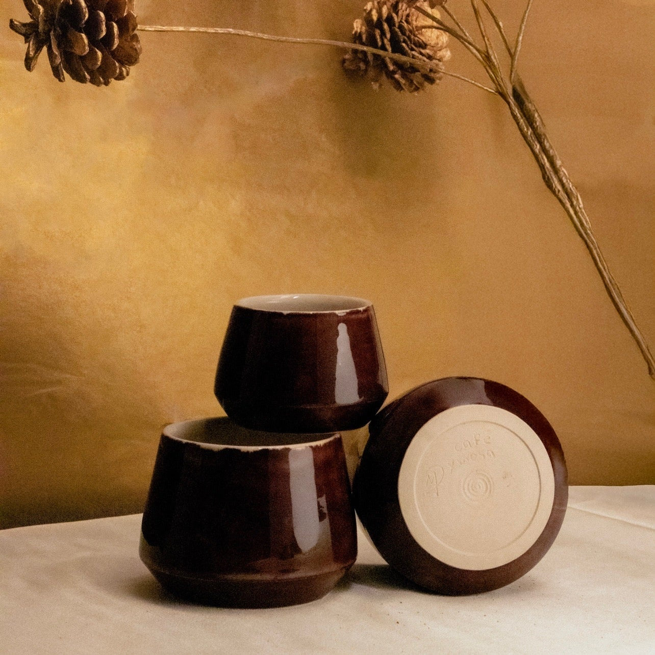 Three dark brown ceramic cups stacked on a light surface with a blurred background